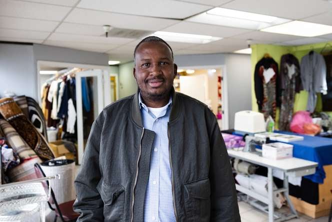 Smiling man wearing a black jacket and blue button down shirt.